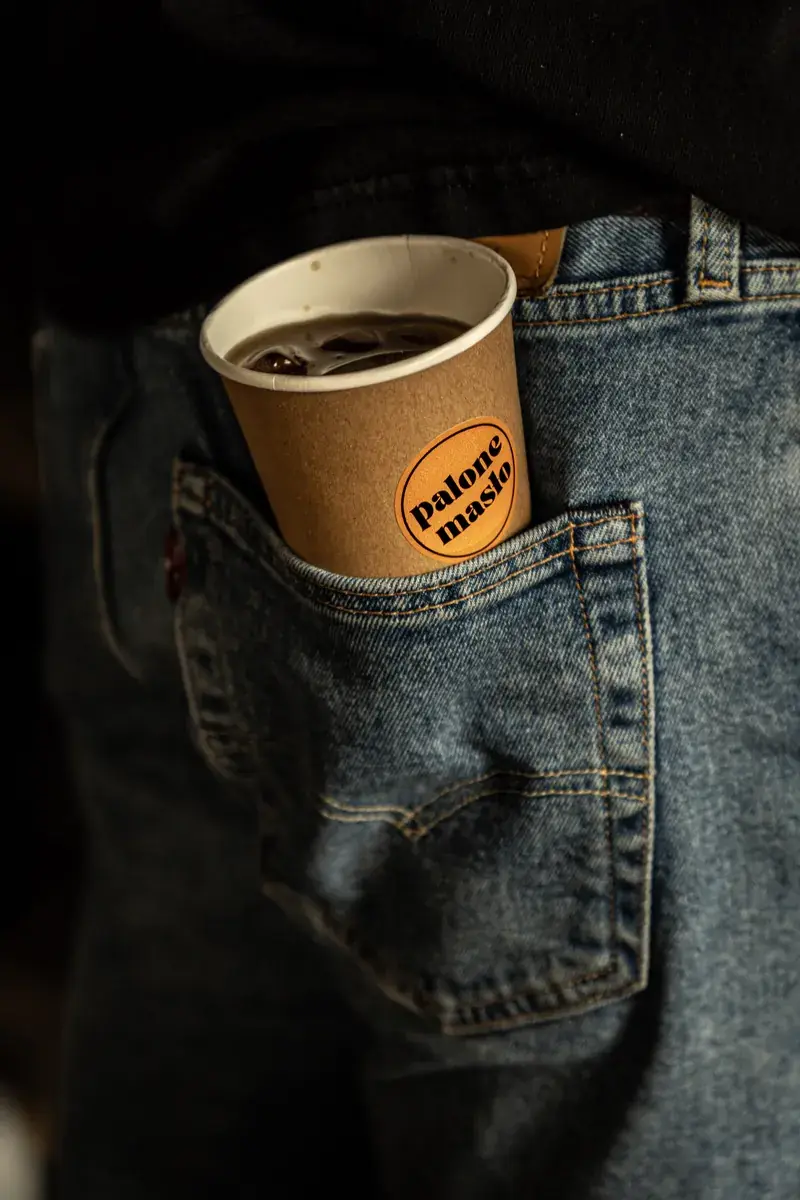 A paper cup with the Palone Masło logo tucked into a jeans pocket