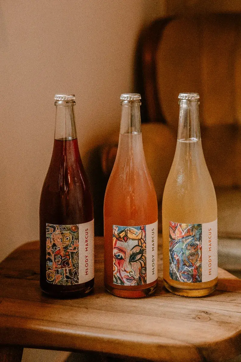 Three bottles of natural wine with colourful labels on a wooden table