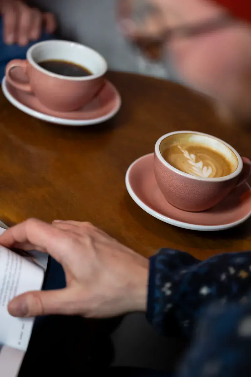 Pink cups of coffee with latte art on a round wooden table, next to an open magazine