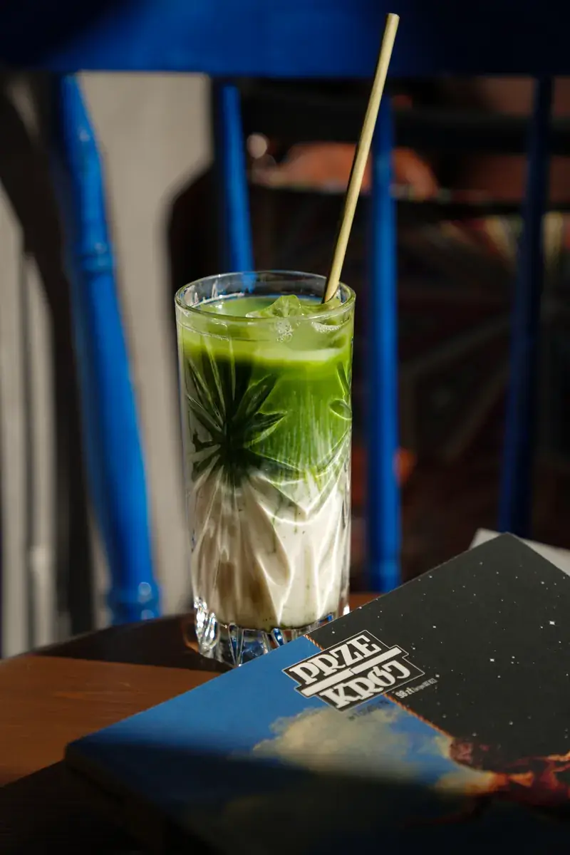 A matcha latte in a cut-glass tumbler with a straw, next to a blue chair and a book