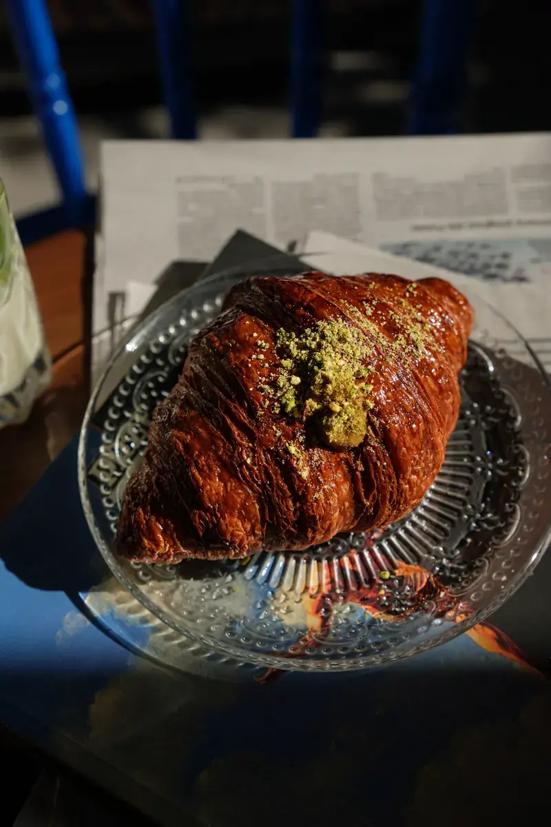 A pistachio croissant on a crystal plate, in sharp afternoon sun
