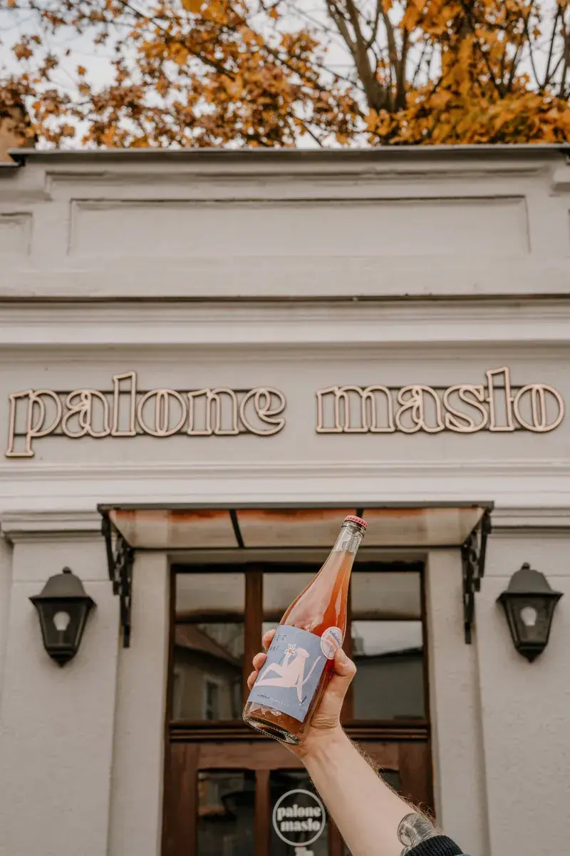The palone masło sign above the café entrance, with a hand holding a bottle in the foreground